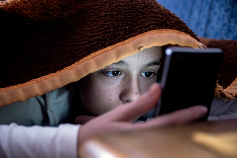 A tired girl using her phone under the blanket